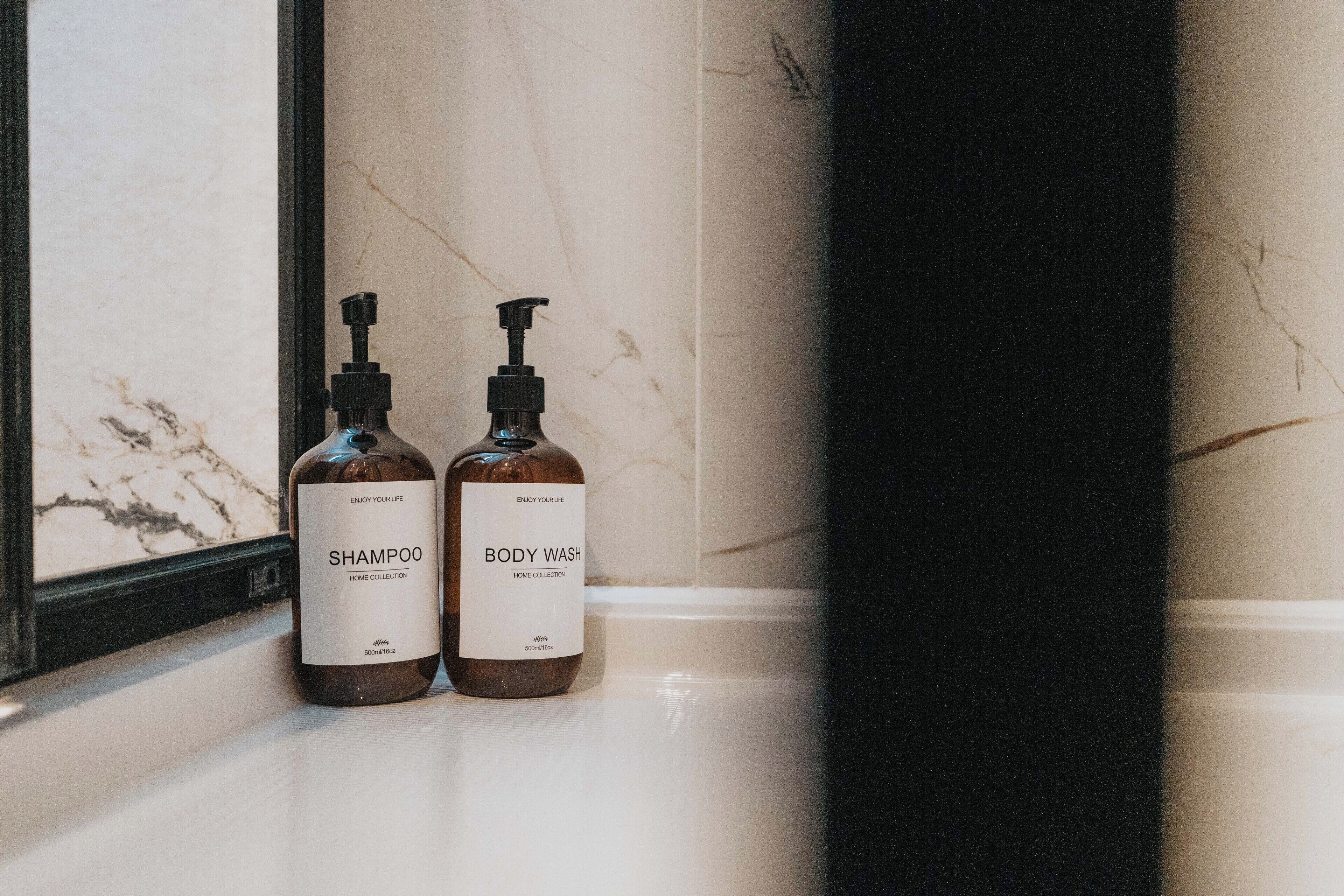 Two bottles of shampoo and body wash on a marble countertop.