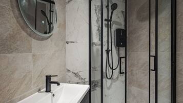 A modern bathroom with a glass-enclosed shower, a round mirror, and a white sink.