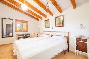 A bedroom with two beds, wooden beams, a mirror, a window, and a dresser.