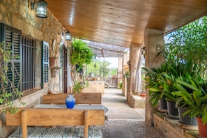 A covered outdoor area with a wooden bench, potted plants, and a stone pathway.