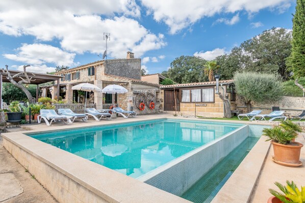 A swimming pool with lounge chairs, a bar, and a rustic building with a tiled roof.