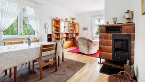 Uma sala de jantar com mesa e cadeiras, uma estante de livros, uma lareira e uma janela com cortinas.