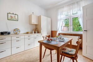A kitchen with a dining table, chairs, cabinets, and a window with curtains.