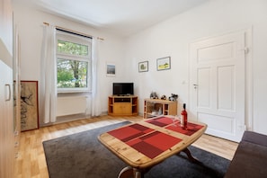 A living room with a wooden table, a television, and a red wine bottle.