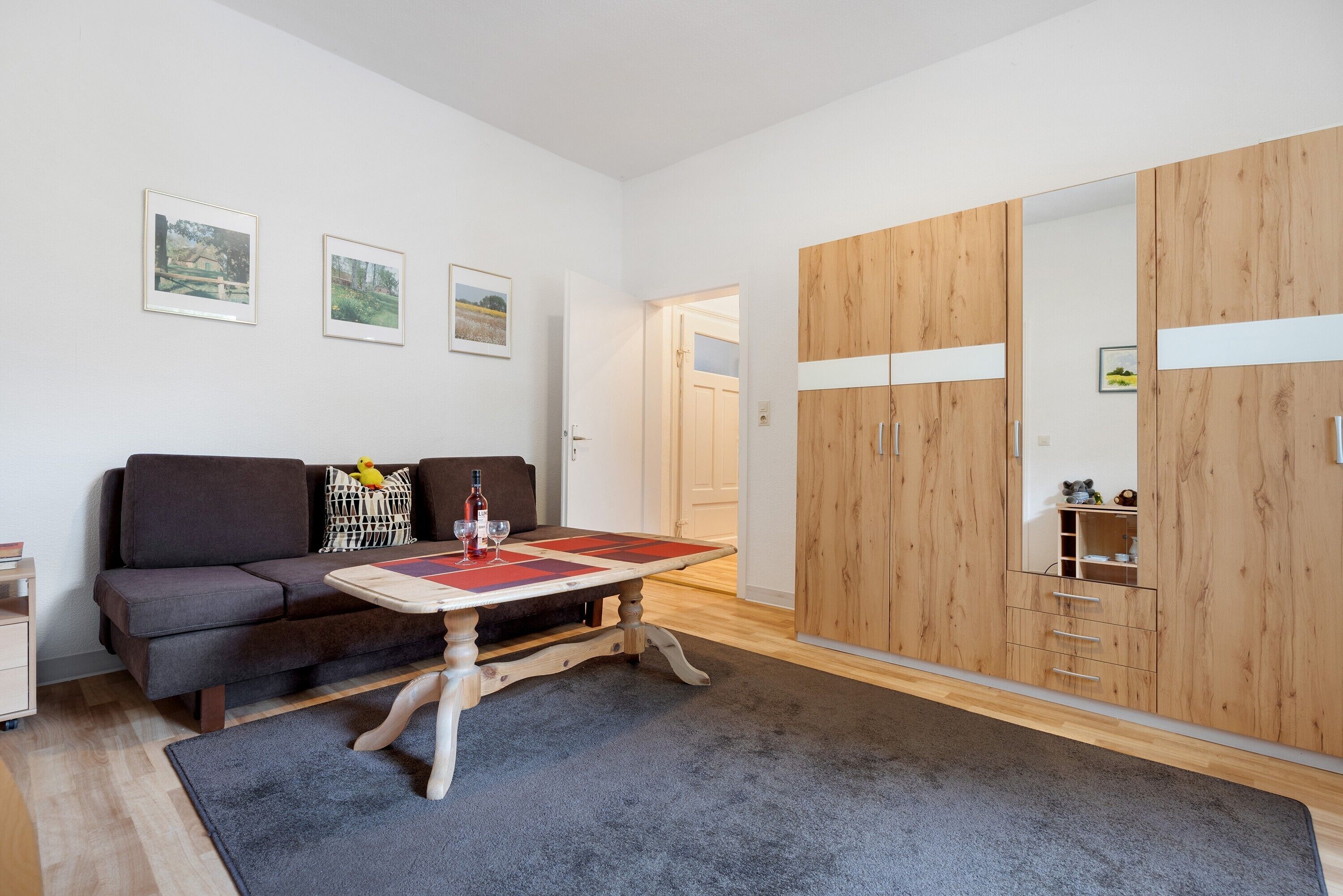 Ein modernes Zimmer mit einer Couch, einem Holzschrank, einem Tisch mit Platzdeckchen und gerahmten Bildern an der Wand.
