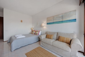 A bedroom with a bed, a sofa, a rug, and a painting on the wall. - Apartment 'Pôr Do Sol' with Sea View, Wi-Fi and Air Conditioning (Alvor)