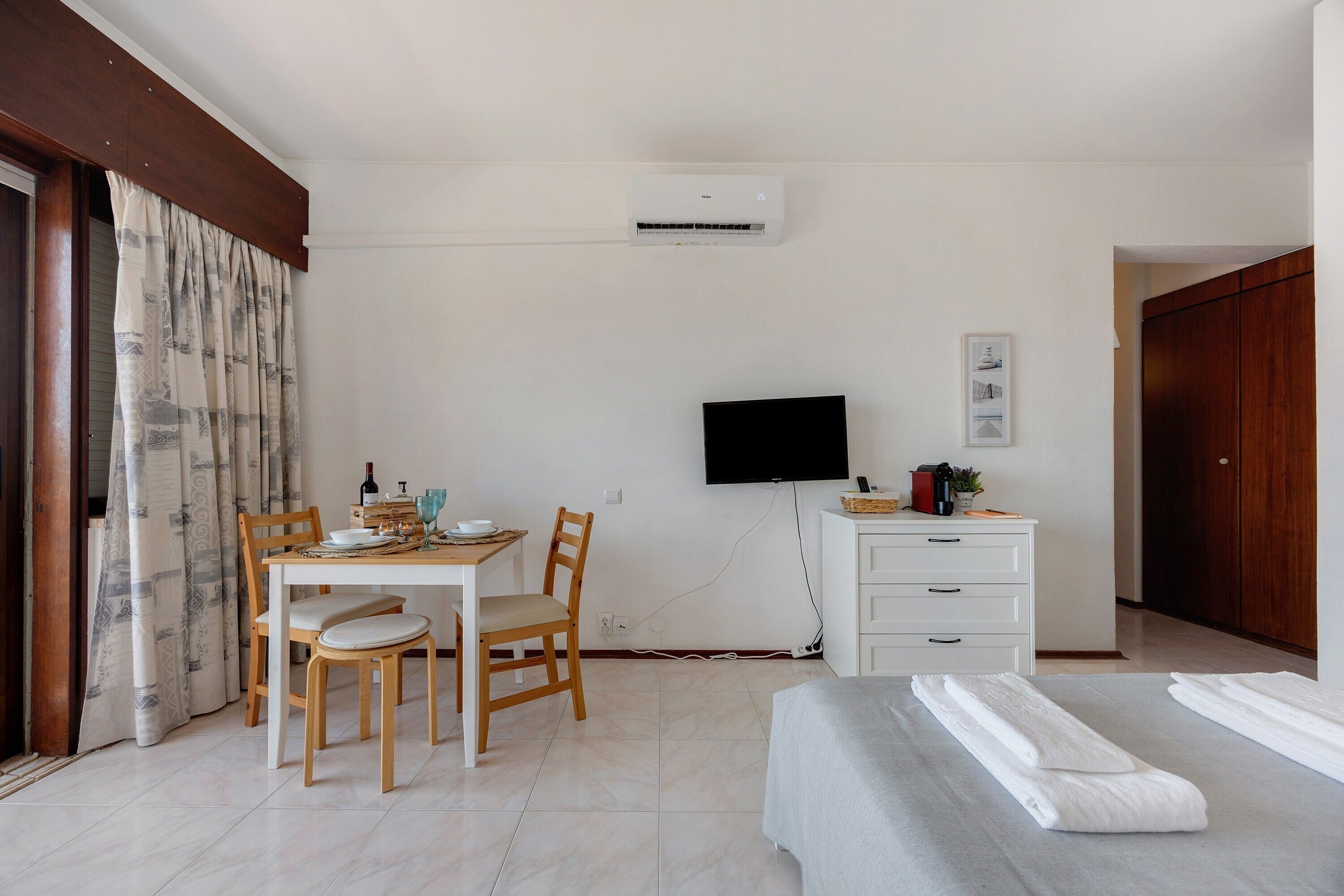 A room with a dining table, chairs, a TV, a bed, and a wardrobe.