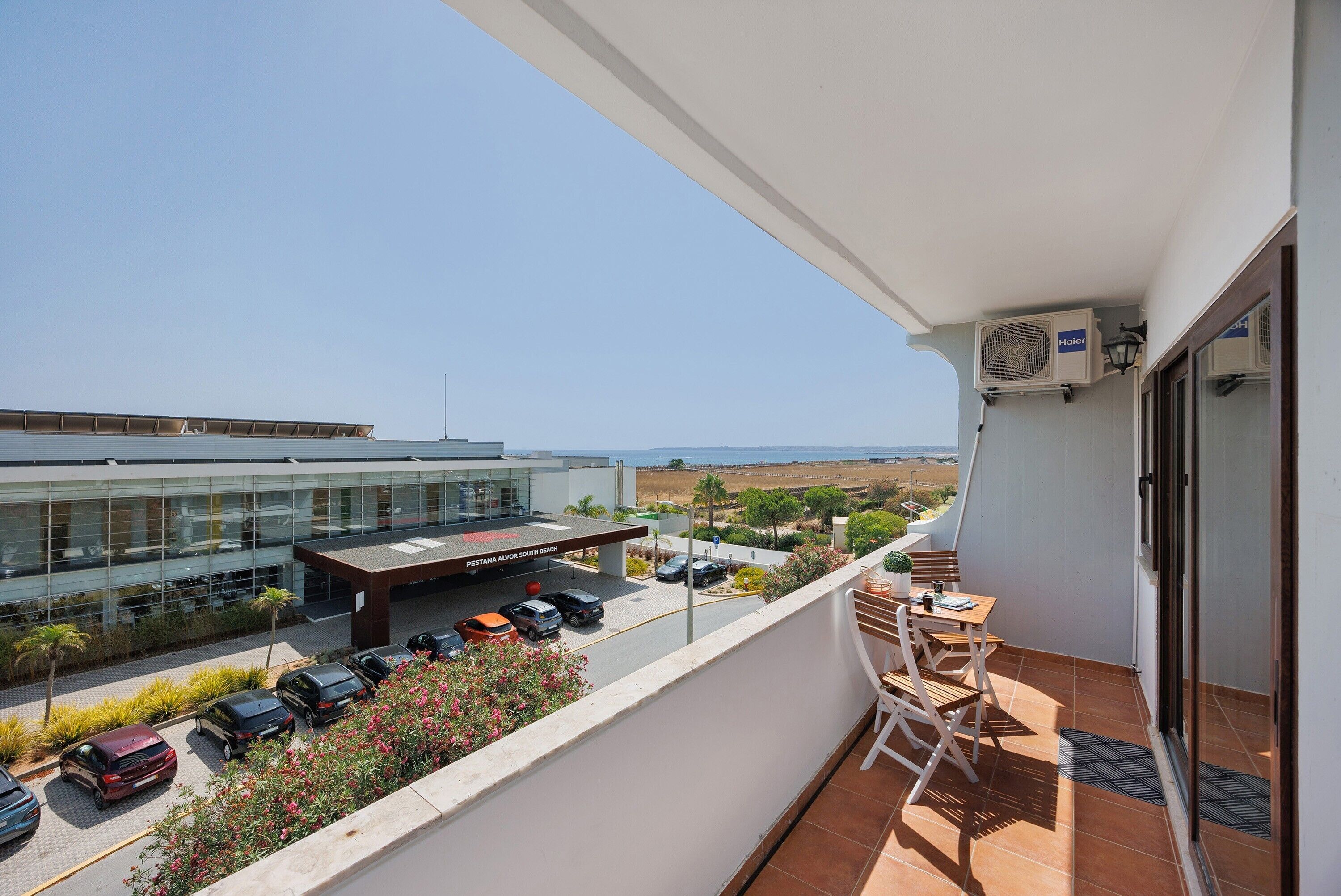 A balcony with a view of a modern building, a parking area, and a clear sky.
