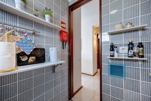 A bathroom with a tiled backsplash, shelves with toiletries, a towel rack, and a door leading to another room. - Apartment 'Pôr Do Sol' with Sea View, Wi-Fi and Air Conditioning (Alvor)