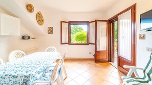 A room with a dining table, chairs, a window with curtains, and a door leading outside. - Three-room apartment "The Flamingos" (Suaredda-traversa)