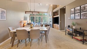 A modern dining area with a large table and chairs, a bookshelf, and a view of the outdoors. - Brighter Days 3 Bedroom Townhouse (Redmond)
