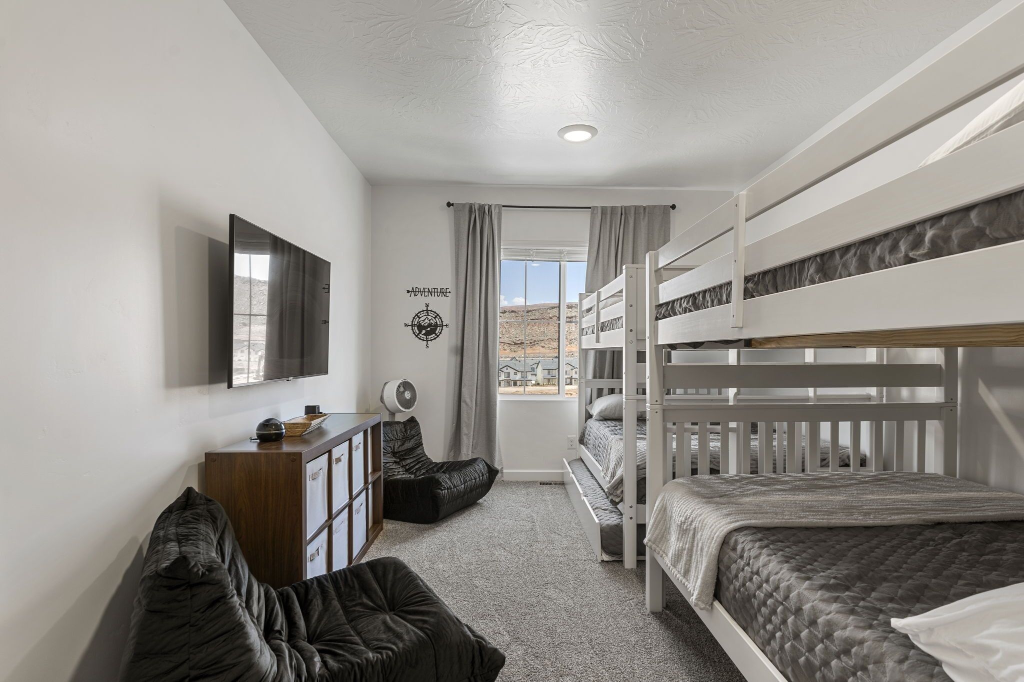 A bedroom with bunk beds, a desk, a chair, and a window with curtains.