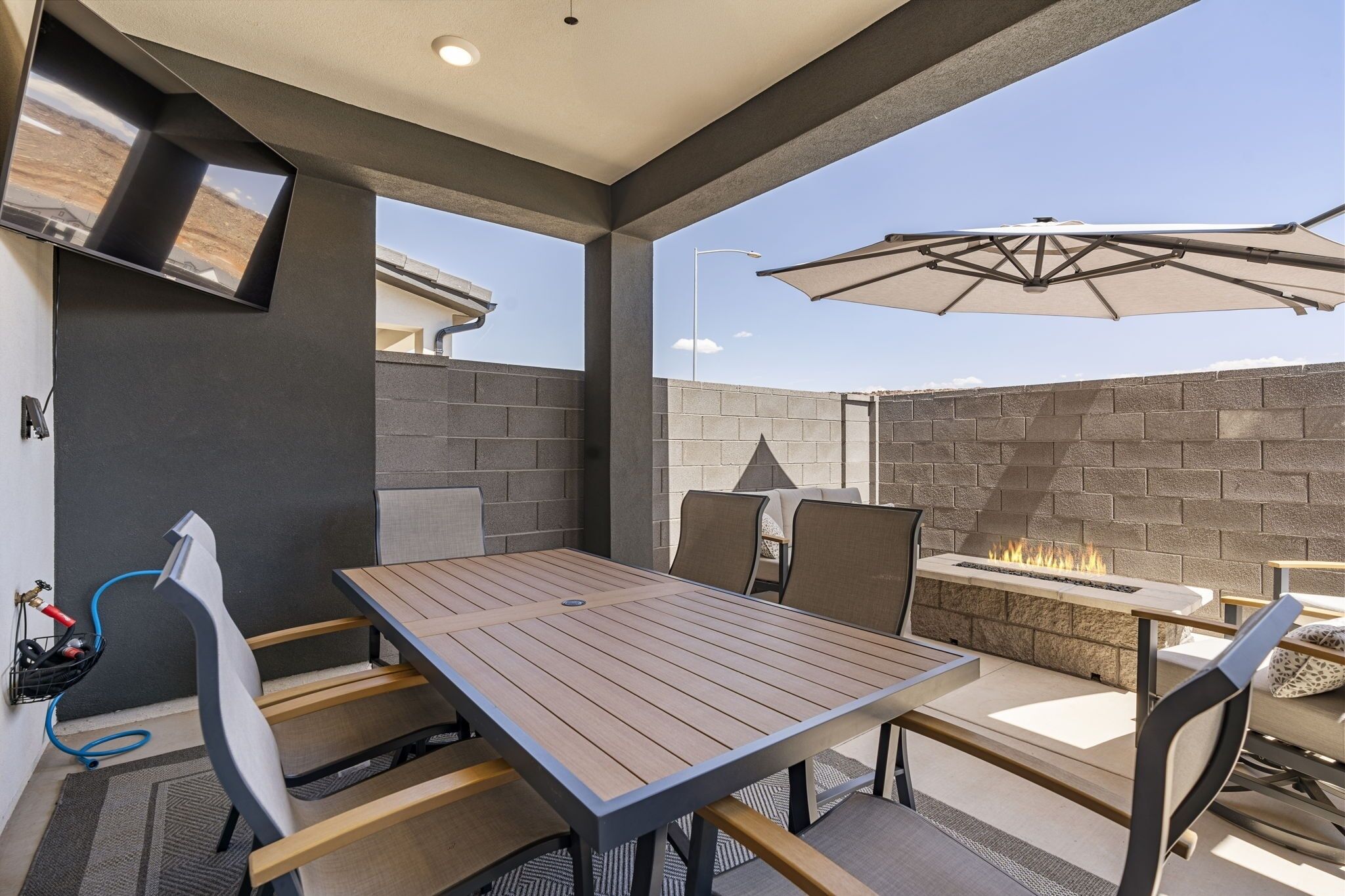 An outdoor patio with a table and chairs, a fire feature, and a mounted TV.