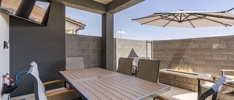 An outdoor patio with a table and chairs, a fire feature, and a mounted TV.