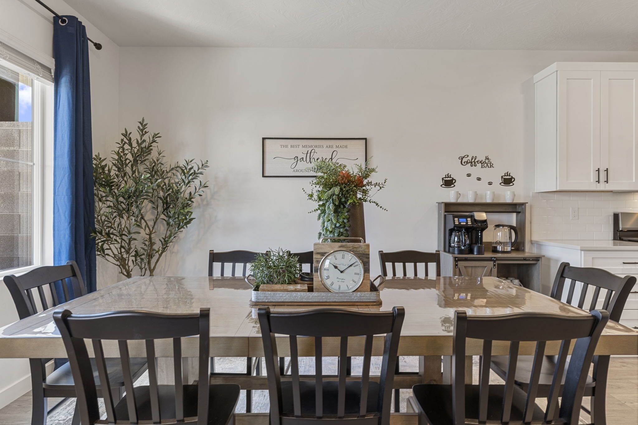 Zona pranzo con tavolo in legno, sedie, orologio e insegna appesa al muro.