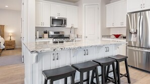 A modern kitchen with white cabinets, stainless steel appliances, a marble countertop, and bar stools.