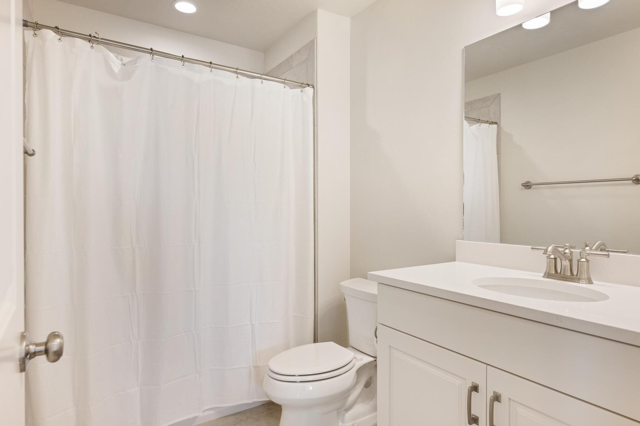 A bathroom with a shower curtain, toilet, sink, and mirror.
