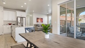 A modern kitchen with white cabinets, a stainless steel refrigerator, and a dining area with a wooden table and chairs.