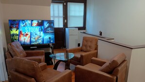 Un salon avec des fauteuils en cuir, une table basse en verre et un téléviseur à écran plat affichant des affiches de films.