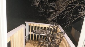 Une terrasse en bois avec une balustrade blanche, une table en métal et deux chaises.