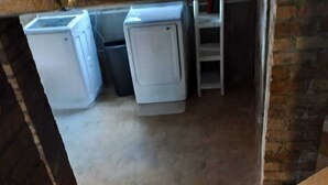 Une buanderie avec deux machines à laver blanches et une poubelle noire.