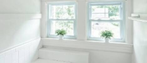 A small, white bathroom with a bathtub, two windows, and a potted plant.