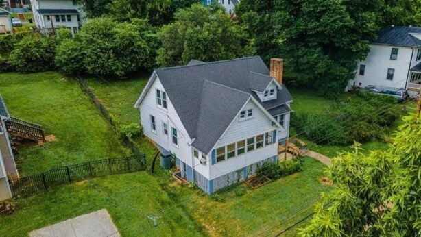 Une maison à deux étages, avec un toit sombre, entourée d’une pelouse bien entretenue et de nombreux arbres.