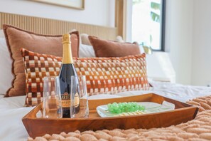 A bed with a wooden tray holding a bottle of champagne, two glasses, and a plate of grapes.