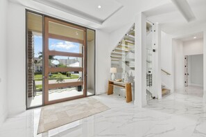 A spacious interior with a large sliding glass door, a wooden bench, and a marble floor. - Ostentatious Home | Short Walk to Beach, Food & Fun (Marco Island)