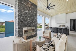 A modern living room with a stone fireplace, comfortable seating, and a view of a swimming pool.