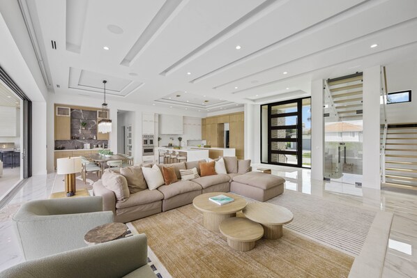 A modern living room with a sectional sofa, a coffee table, and a dining area with a kitchen in the background.