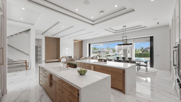 A modern kitchen with a large island, wooden cabinets, and a view of a marina.