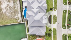 An aerial view of a building with a geometric roof design, adjacent to a body of water and a landscaped area with pathways and greenery.