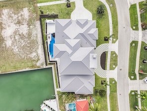 An aerial view of a building with a geometric roof design, adjacent to a body of water and a landscaped area with pathways and greenery.