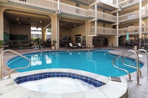 A swimming pool with a hot tub, lounge chairs, and a covered patio area.