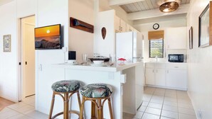 Une cuisine moderne avec des meubles blancs, un îlot central doté de tabourets, un téléviseur fixé au mur et un élément décoratif mural.
