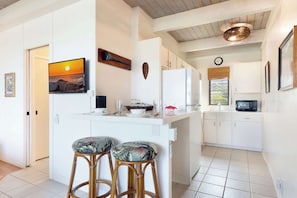 A modern kitchen with white cabinetry, a central island with stools, a mounted TV, and a decorative wall piece.