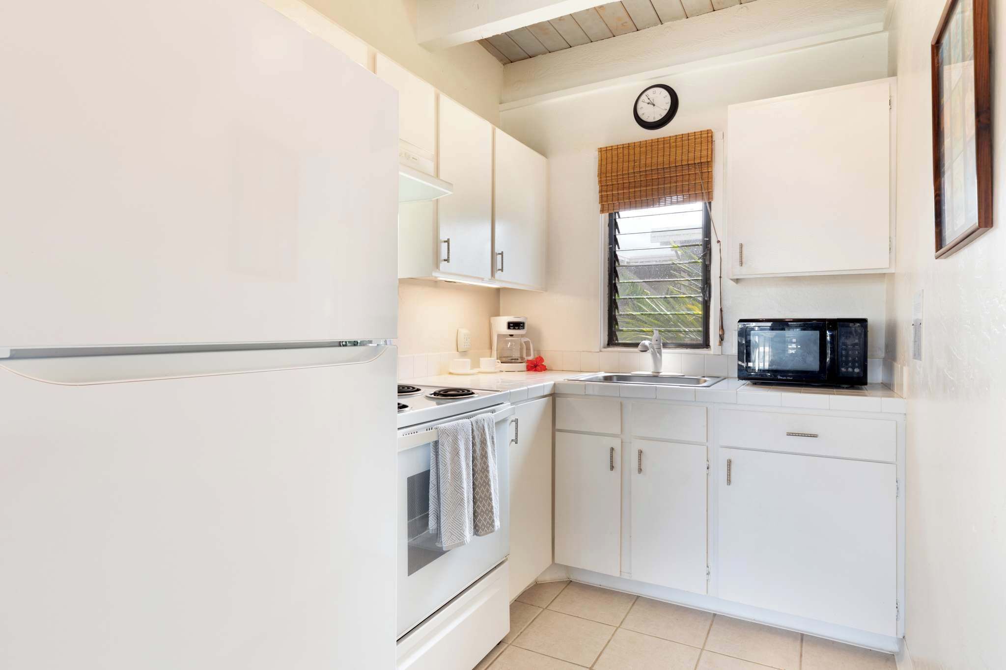 A compact kitchen with white cabinets, a stove, a microwave, and a clock on the wall.