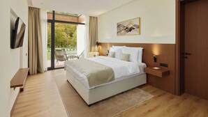 A modern hotel room with a large bed, a TV, a wooden nightstand, a desk, and a sliding glass door to the outdoors. - Terra Homes (Kolasin)