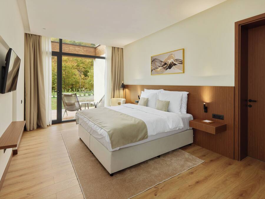 Una habitación de hotel moderna con una cama grande, televisión, mesita de noche de madera, escritorio y puerta corrediza al exterior.