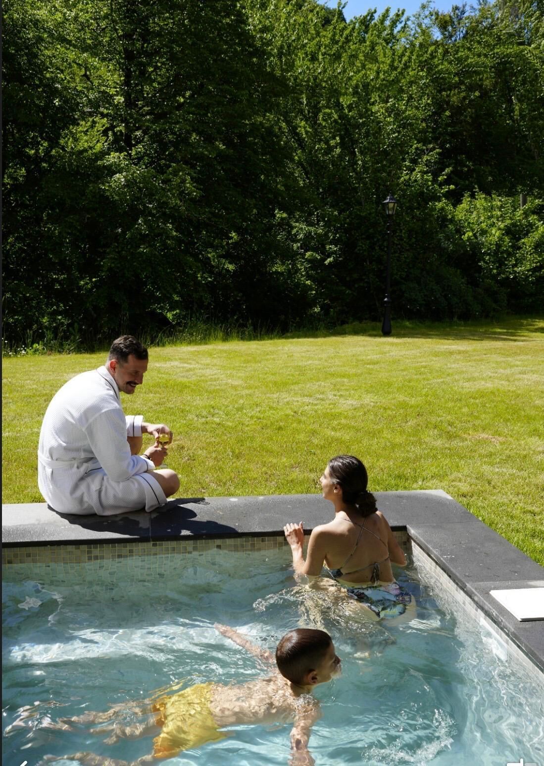 A swimming pool with a tiled edge, surrounded by a grassy area and trees.