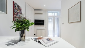Un salon moderne avec une table blanche, une plante en pot, un téléviseur à écran plat et un radiateur.