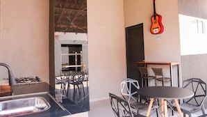 A kitchen with a gas stove, a sink, and a grill. There is a table with chairs and a guitar hanging on the wall. - Casa com Garagem e Churrasqueira em Tima Regi o (Olímpia)