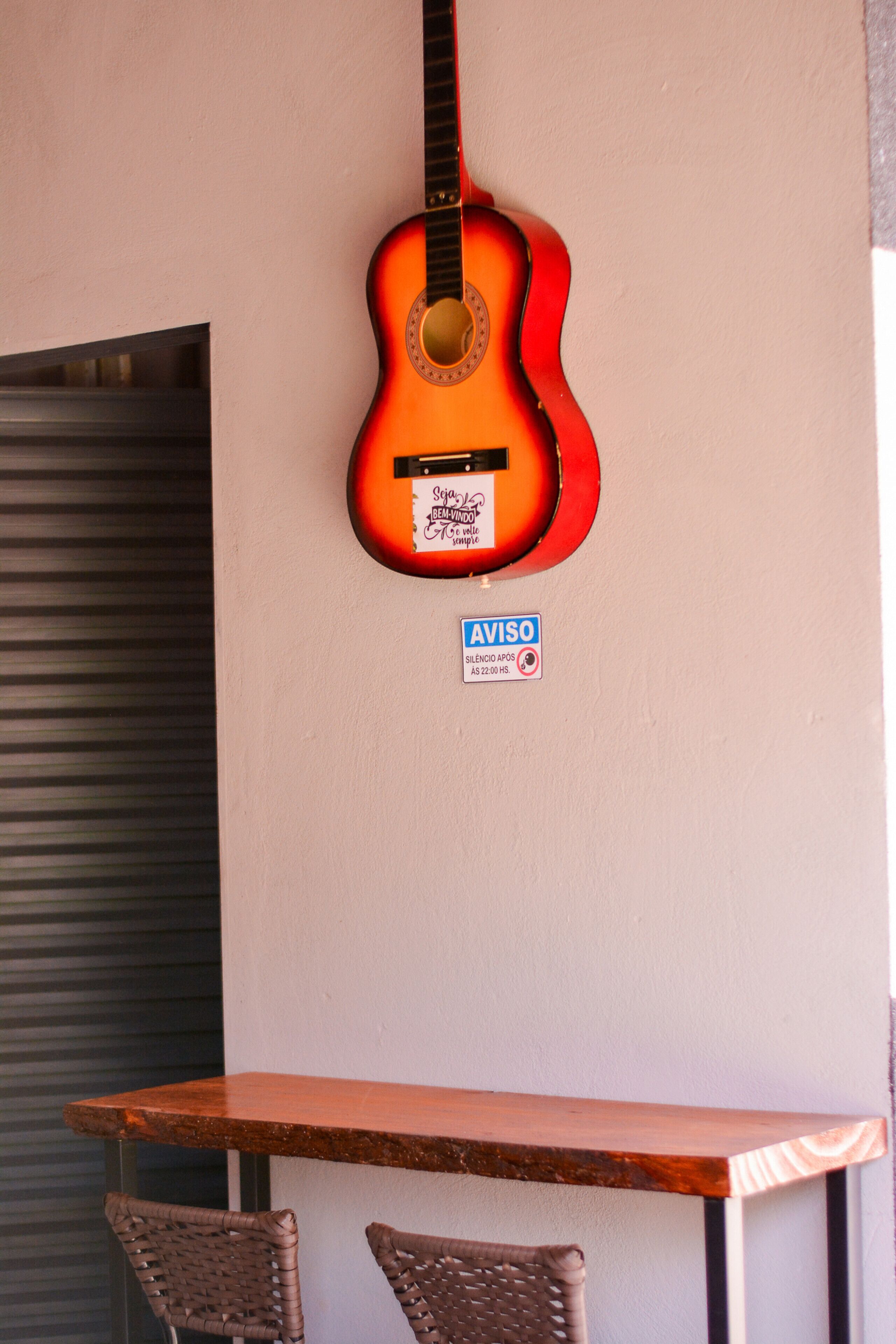 A guitar hanging on a wall, a table, and two wicker chairs.