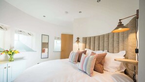 A modern bedroom with a large bed, a bedside table, a lamp, and a mirror.