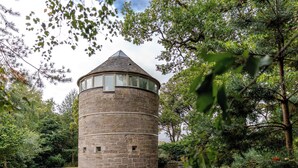 A stone tower with a conical roof, surrounded by dense greenery.