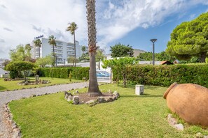 Un jardin aménagé avec un palmier, un grand pot de fleurs et un bâtiment doté de balcons en arrière-plan.
