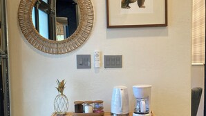 Une console en osier, sur laquelle se trouvent une machine à café, un tableau encadré représentant un animal et un miroir accroché au mur.