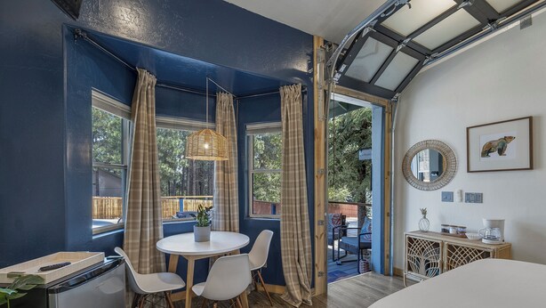 Une pièce comprenant un lit, une table à manger avec des chaises, un petit coin cuisine, une fenêtre avec des rideaux et une vue sur l’extérieur.