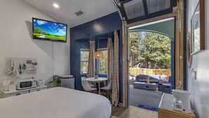 Une chambre avec un lit, une télévision, un bureau doté d’un micro-ondes, et une vue sur une terrasse extérieure aménagée avec un canapé et un foyer.